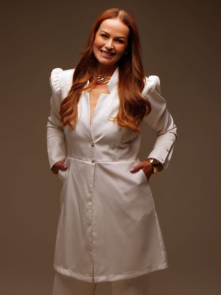 Simone Dante, biomédica esteta, de jaleco branco e braços cruzados, sorrindo